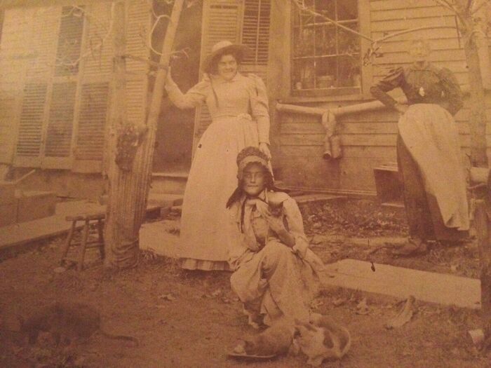 Sepia-toned vintage photo showing three women in old-fashioned dresses with cats, eerie and creepy past image.