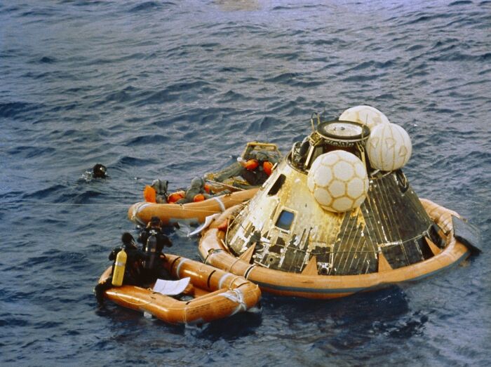 Apollo mission capsule floating in the ocean with rescue divers and flotation devices during recovery operation.