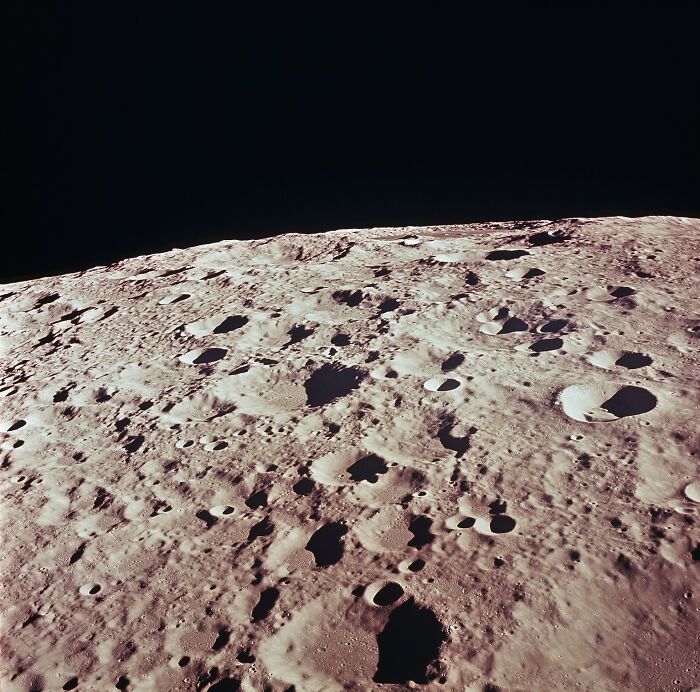 Lunar surface filled with craters captured in iconic Apollo mission photo showing the moon’s rugged terrain against black space.