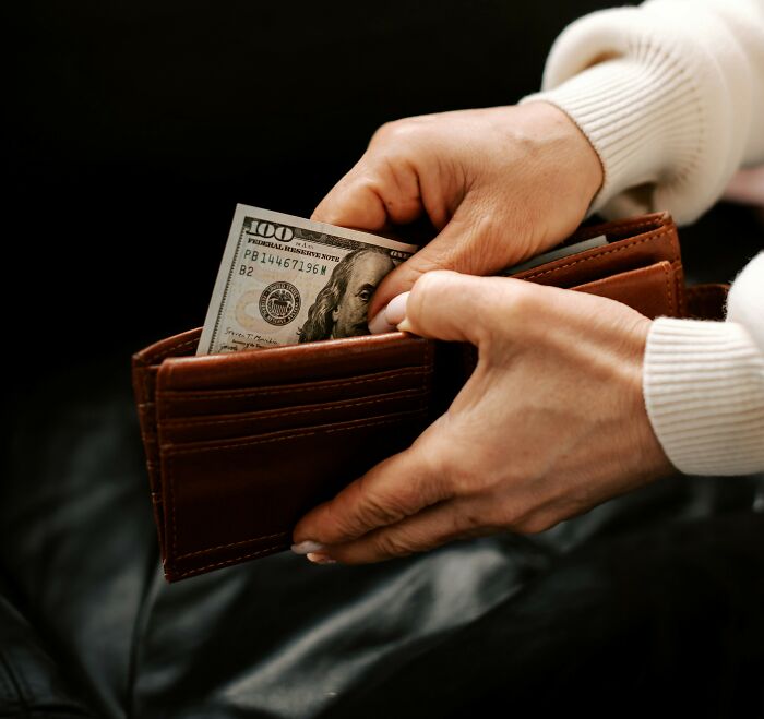 Hands placing a 100-dollar bill into a brown wallet, depicting a relatable middle class money moment.