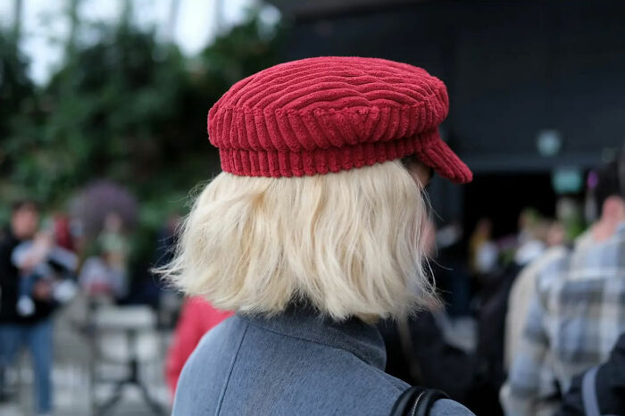 Person with blonde hair wearing a red hat in a busy urban setting, a beautiful street shot capturing everyday life poetry.