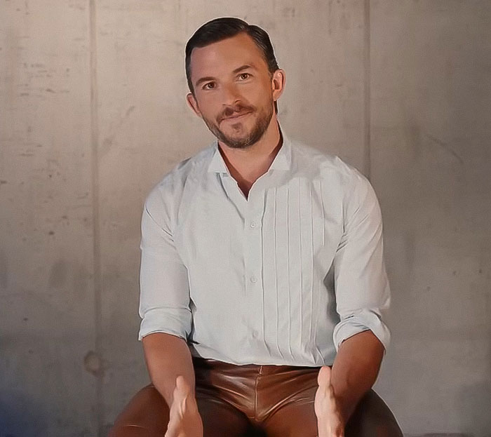 Man in a white shirt and brown pants sitting against a plain wall, posing with hands slightly raised and smiling. Man in a white shirt and brown pants sitting against a plain wall, posing with hands slightly raised and smiling.