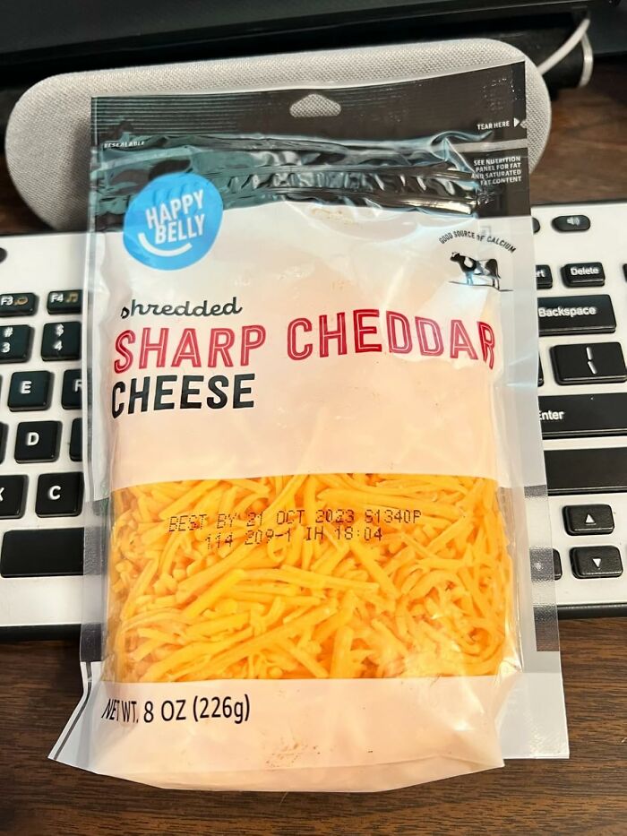Shredded sharp cheddar cheese package on keyboard highlighting Amazon Fresh staples cheaper than big box stores.