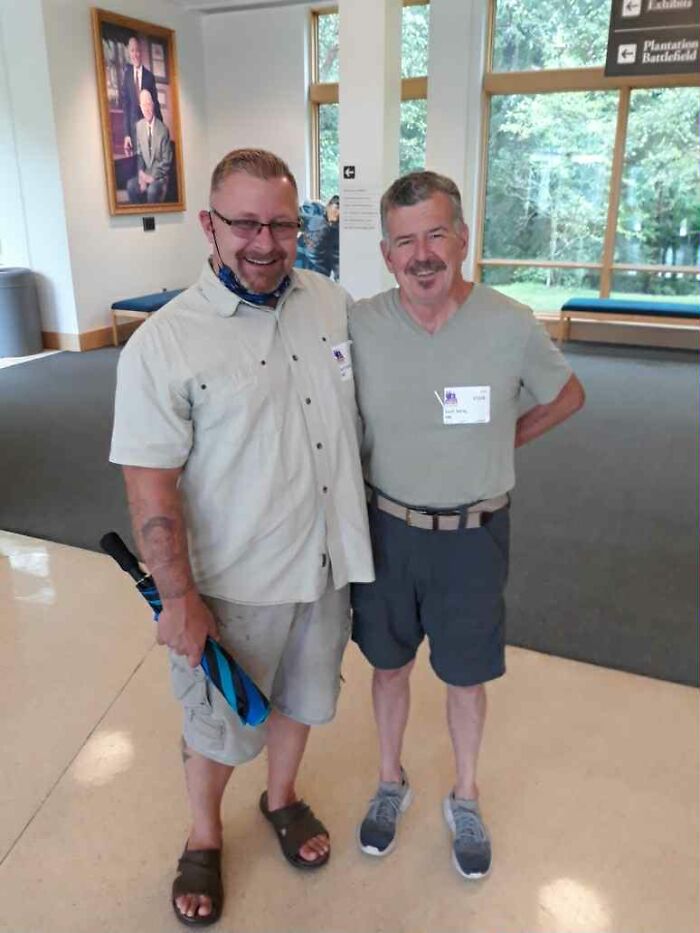 Two men standing together indoors, smiling and wearing casual clothes, connected by a shared teddy bear heartbeat story.