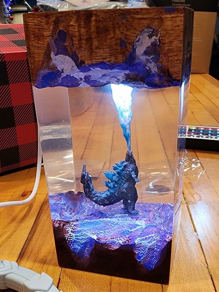 Bizarre find of Godzilla figurine emitting blue light inside a clear resin block on wooden floor surface.
