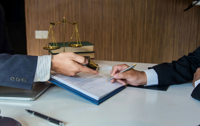 Two men in suits reviewing documents on a table with legal scales and books, related to hired PI findings. Two men in suits reviewing documents on a table with legal scales and books, related to hired PI findings.