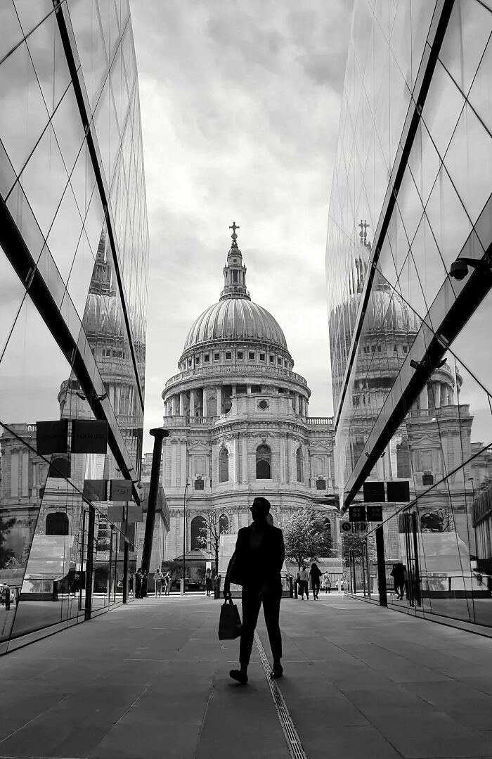 Silhouette of a person walking between reflective buildings with a historic dome in the background, a beautiful street shot capturing everyday life.