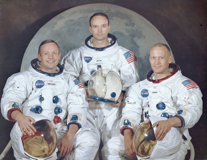 Apollo mission astronauts wearing space suits posing in front of a moon backdrop in an iconic space photo.