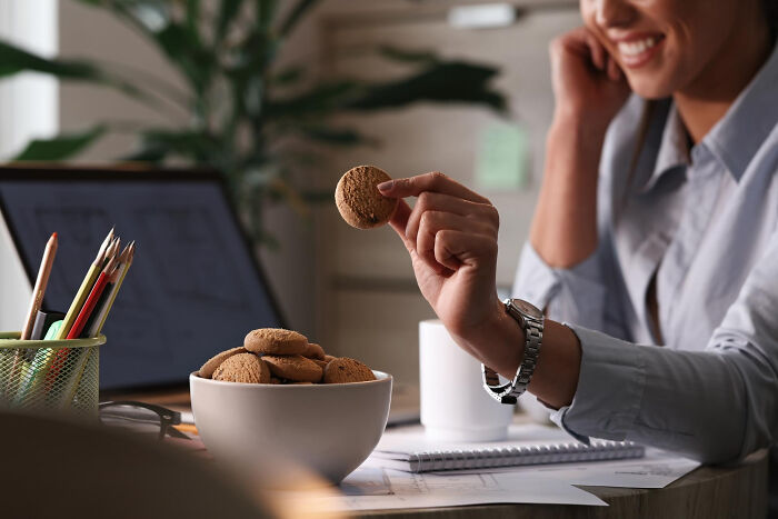 Woman smiling while holding a cookie at a desk, enjoying a small reward after spending just a dollar.