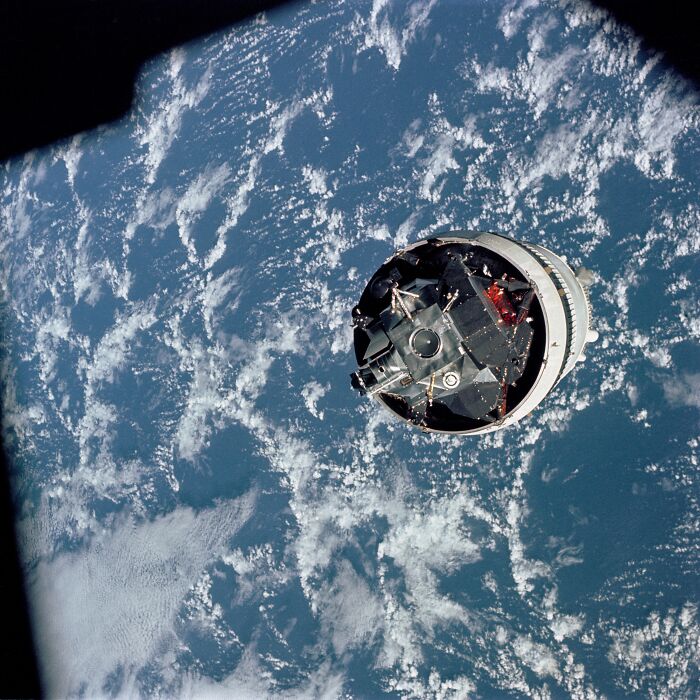Apollo mission spacecraft orbiting above Earth with clouds and ocean visible beneath in stunning space photo.