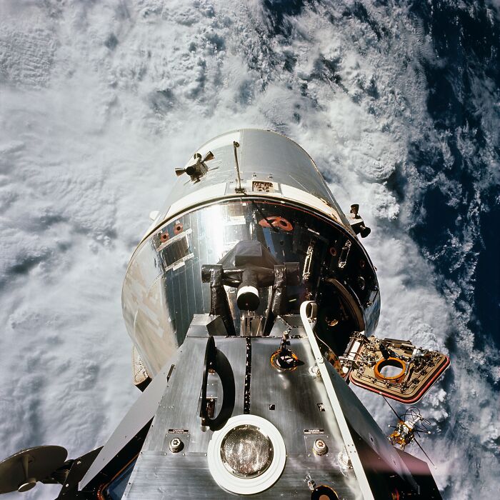 Apollo mission spacecraft orbiting Earth with detailed surface and cloud patterns visible below in space.
