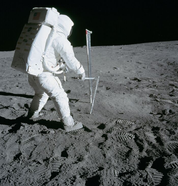 Apollo mission astronaut collecting lunar soil samples on the moon’s surface with footprints visible in the dust.