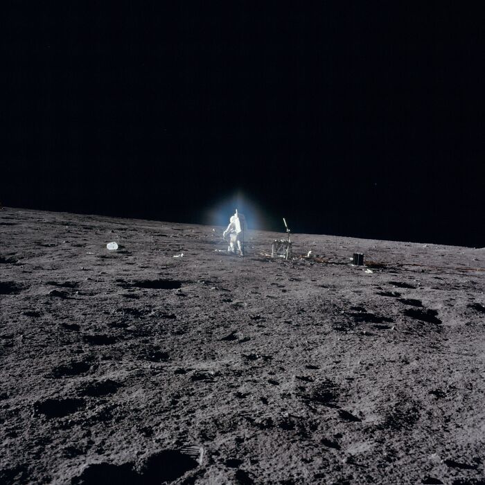 Apollo mission photo showing astronaut on the moon with lunar surface and deep black space background.