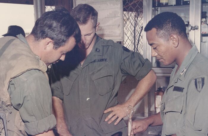 Three soldiers, including an African American serviceman, in military uniforms reviewing equipment indoors, highlighting African American military history.