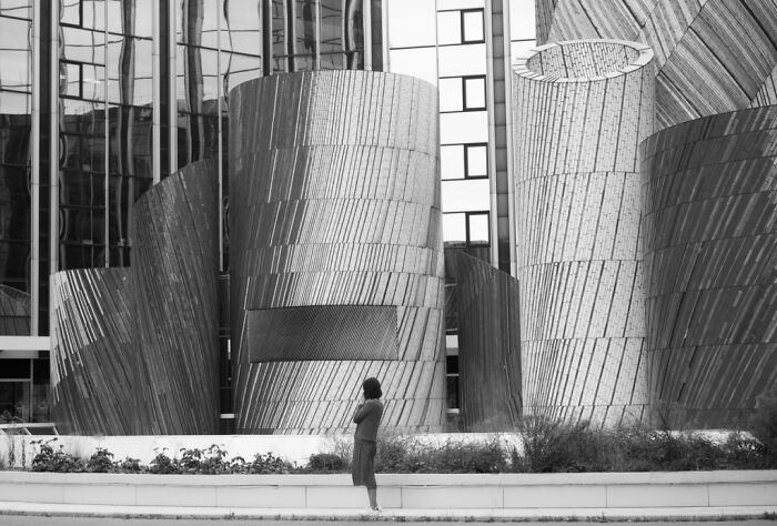Woman standing near large modern metallic architectural sculptures in a cinematic photo capturing everyday life moments.