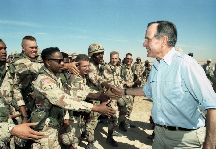 Former President George H.W. Bush shaking hands with African American military personnel during an outdoor event.