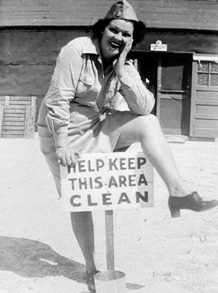 Vintage black and white photo of a woman in uniform posing with a sign in a confusing historic scene.