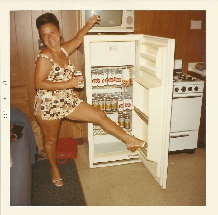 Woman in vintage dress posing with open refrigerator filled with beer cans, showcasing confusing history in old photos.