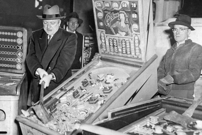 Men in vintage clothing playing an old pinball machine in a historical scene from the confusing history pics collection.