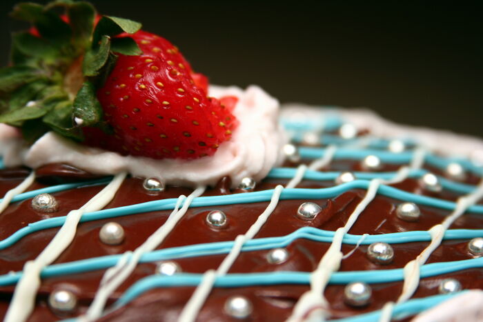 Close-up of a chocolate dessert with decorative icing and a fresh strawberry highlighting surprising foods banned in the USA.