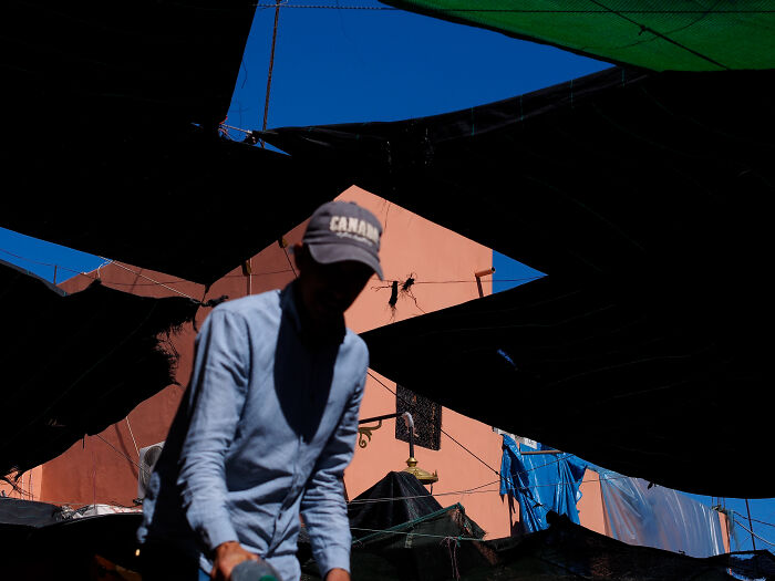 Silhouetted photographer capturing candid street moments beneath fabric canopies with vibrant buildings and clear sky background.