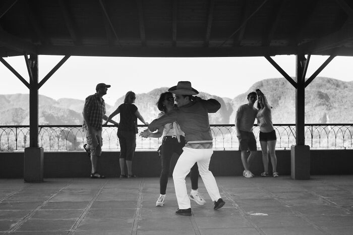 Black and white cinematic photo capturing people dancing and socializing on a covered terrace with a mountain backdrop.