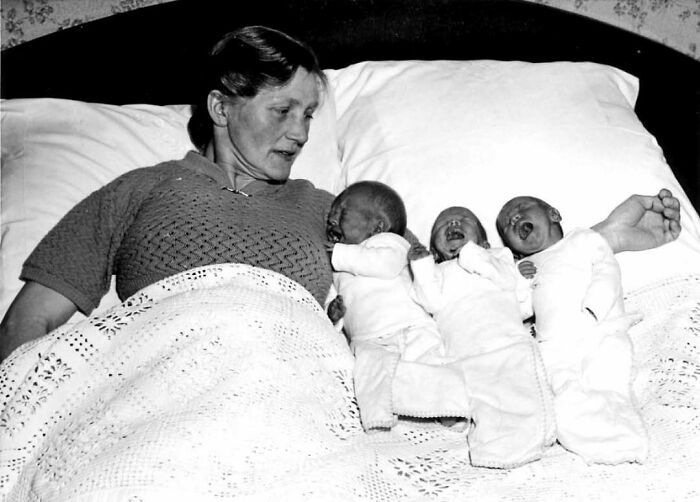 Mother lying in bed with three newborn babies, a historical photo showing family life in confusing old pics.