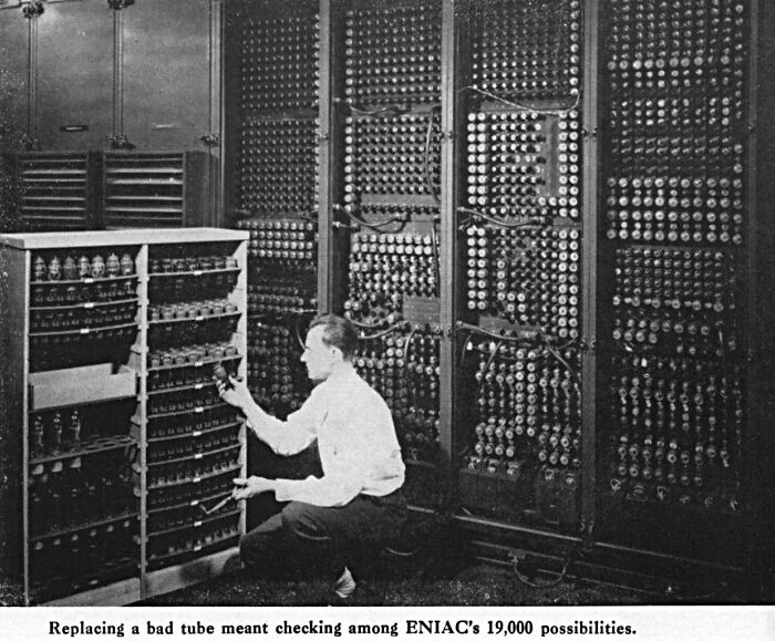 Man working on an early computer with numerous tubes and dials, illustrating theories about the afterlife concept.
