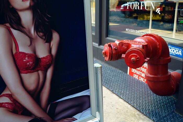 Street photography capturing a red fire hydrant seemingly interacting with a lingerie ad, highlighting magical city life coincidences.
