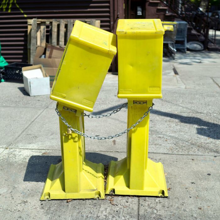 Two yellow newspaper boxes chained together on a city sidewalk, capturing a street photographer's coincidence in urban life.