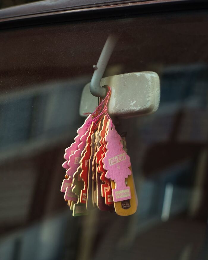 Close-up of multiple air fresheners hanging from a rearview mirror, showcasing a street photographer's captured coincidence.