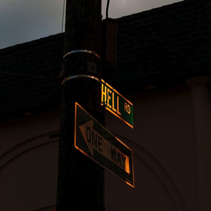 Street photographer captures magical city life with coincidence in illuminated street signs at dusk on Hell Road.