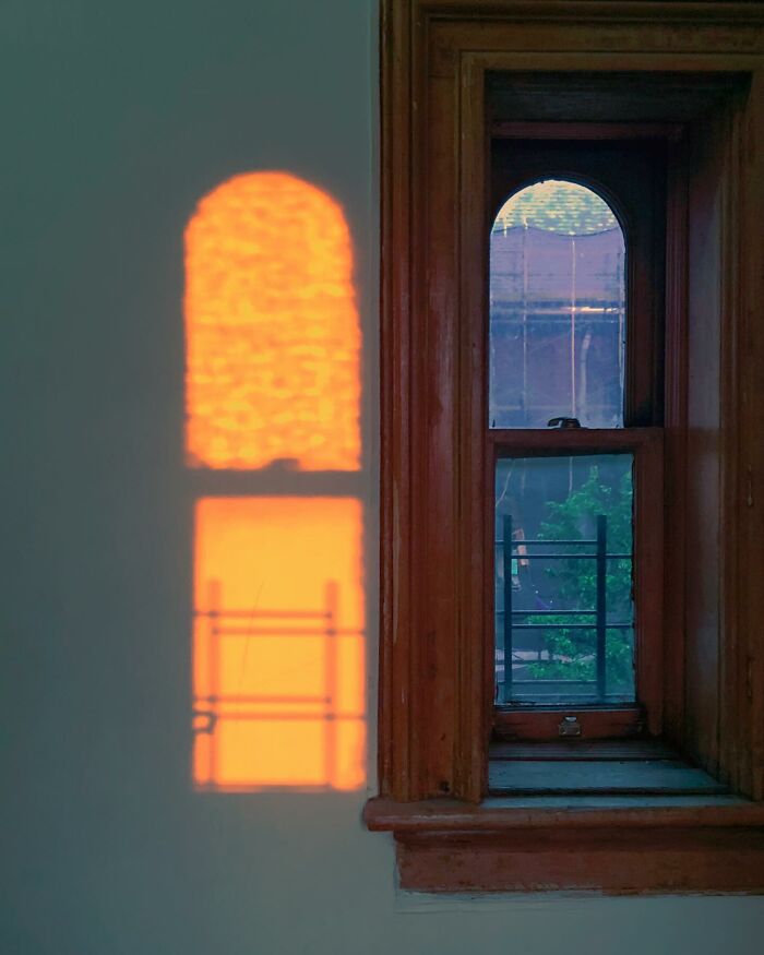 Shadow reflection from an arched window with wooden frame, showcasing city life and street photographer's magical coincidence capture.