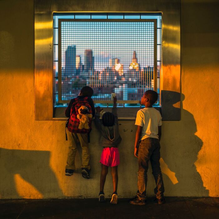 Three children looking through a metal grid window at a cityscape, captured in a street photographer's magical city life scene.