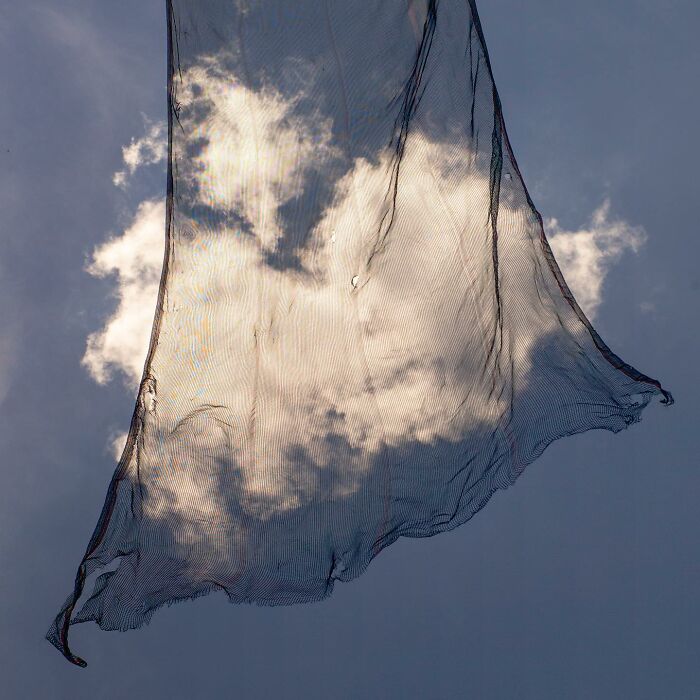 A street photograph capturing a translucent net against a blue sky with clouds, showcasing magical city life coincidences.