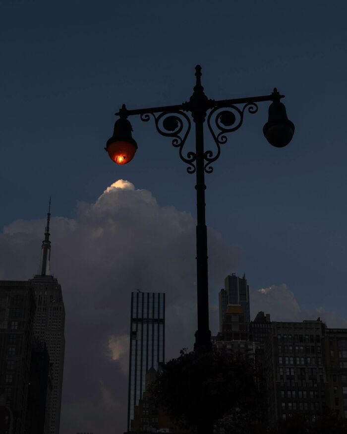 Street photographer captures a magical city moment with a glowing lamp post against a dark urban skyline at dusk.