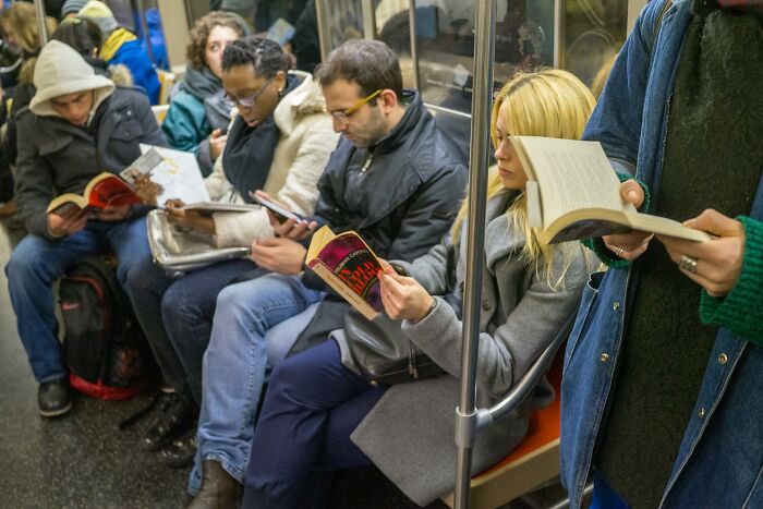 Commuters reading books and using phones on a crowded subway, capturing street photographer's city life coincidences.