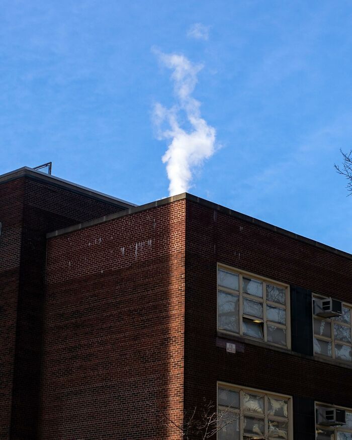 Street photographer captures a red brick building with smoke curling upwards under a clear blue sky in a city scene.