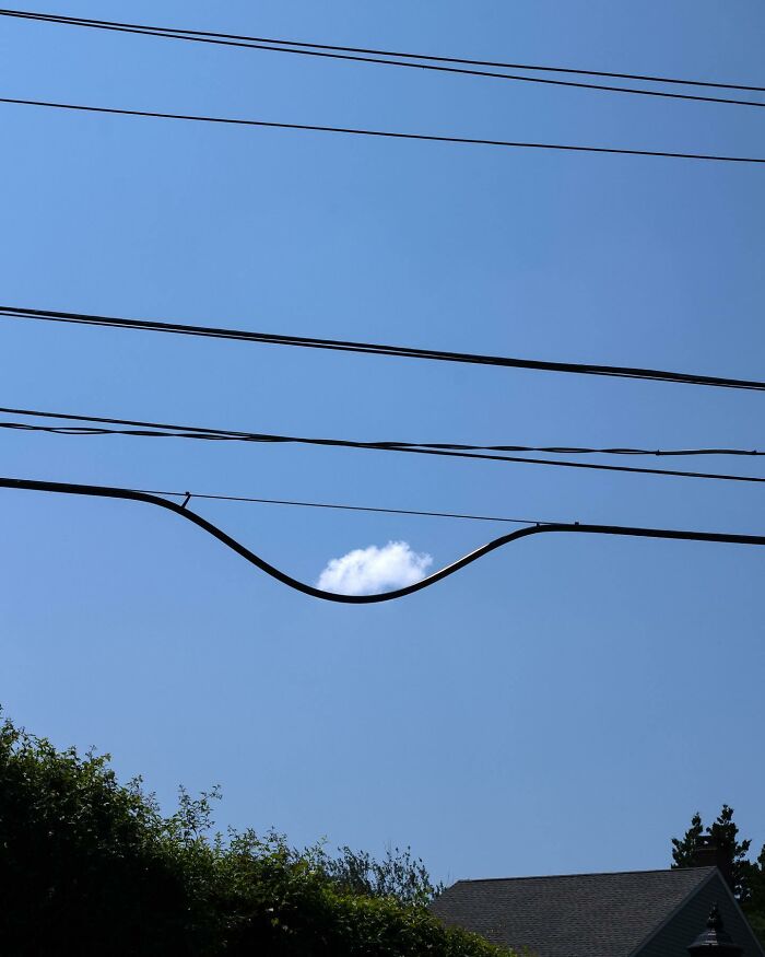 Street photographer captures coincidence of a cloud perfectly framed by city power lines against blue sky.
