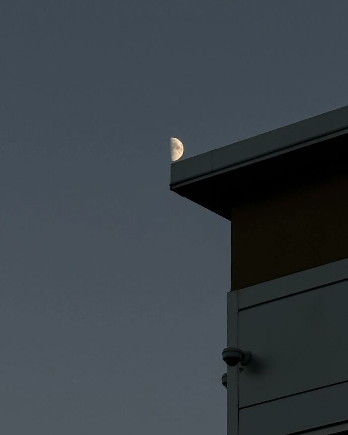 Half moon appearing to rest on the edge of a building roof, showcasing a magical street photography coincidence in city life.