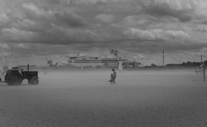Black and white cinematic photo by Adriana Ferrarese showing a solitary person on a chair in a foggy, open landscape with a distant ship.