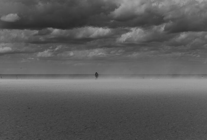 Cinematic photo of a lone figure walking on a vast misty plain under a dramatic cloudy sky by Adriana Ferrarese.