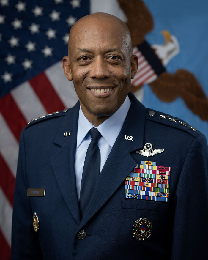 African American military officer in decorated uniform smiling with American flag and eagle emblem background.
