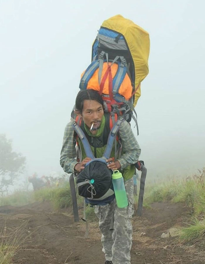Mountain guide carrying large backpack climbing foggy trail during active volcano body recovery mission. Mountain guide carrying large backpack climbing foggy trail during active volcano body recovery mission.