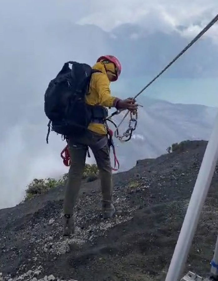 Rescuer in yellow jacket and helmet descending active volcano with rope during body recovery from 1600ft-deep site. Rescuer in yellow jacket and helmet descending active volcano with rope during body recovery from 1600ft-deep site.