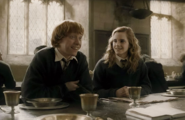 Emma Watson and co-star sitting at a Hogwarts dining table in a Harry Potter film scene. Emma Watson and co-star sitting at a Hogwarts dining table in a Harry Potter film scene.