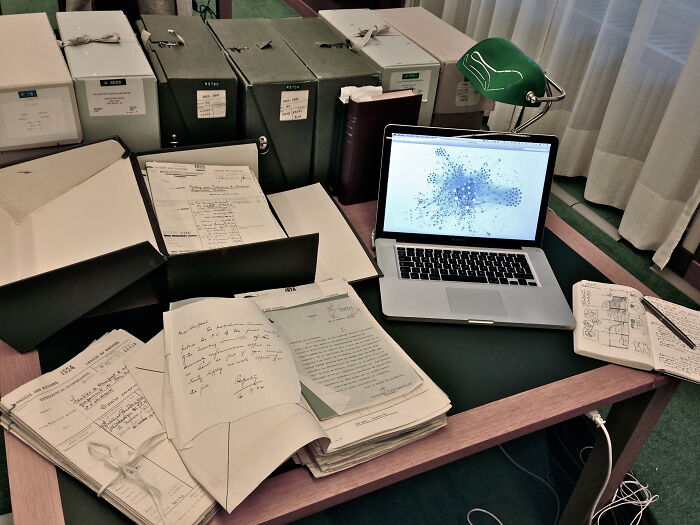 Desk with old documents, files, and a laptop displaying data visualization for afterlife theories research.