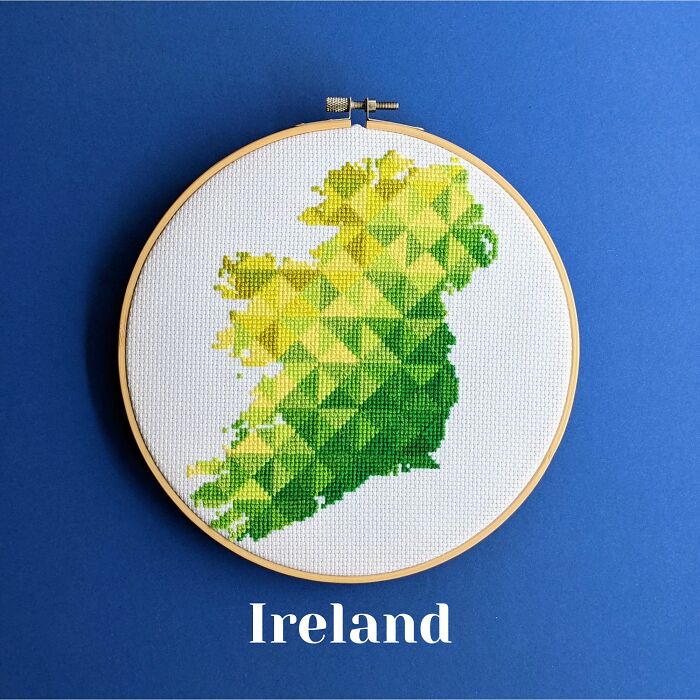 Cross-stitched map of Ireland in green and yellow shades displayed in an embroidery hoop on a blue background.