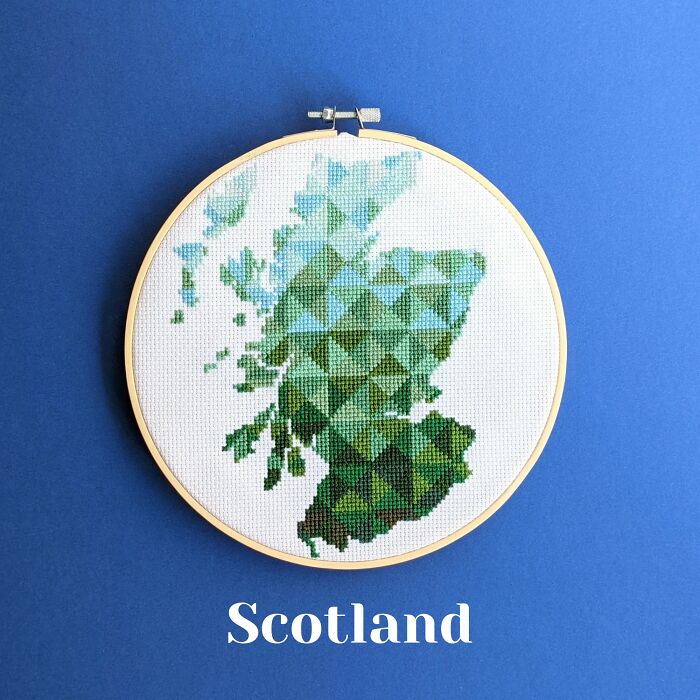 Cross-stitched map of Scotland in shades of green and blue displayed in an embroidery hoop on a blue background.