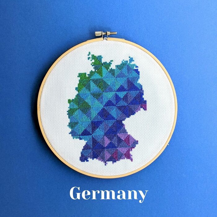 Cross-stitched map of Germany in blue and green hues displayed in an embroidery hoop on a blue background.